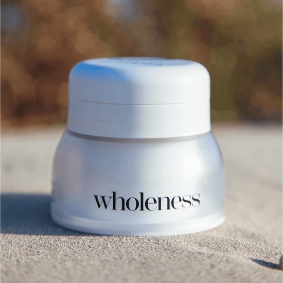 White jar labeled 'wholeness' on a sandy surface with a blurred natural background