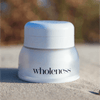 White jar labeled 'wholeness' on a sandy surface with a blurred natural background