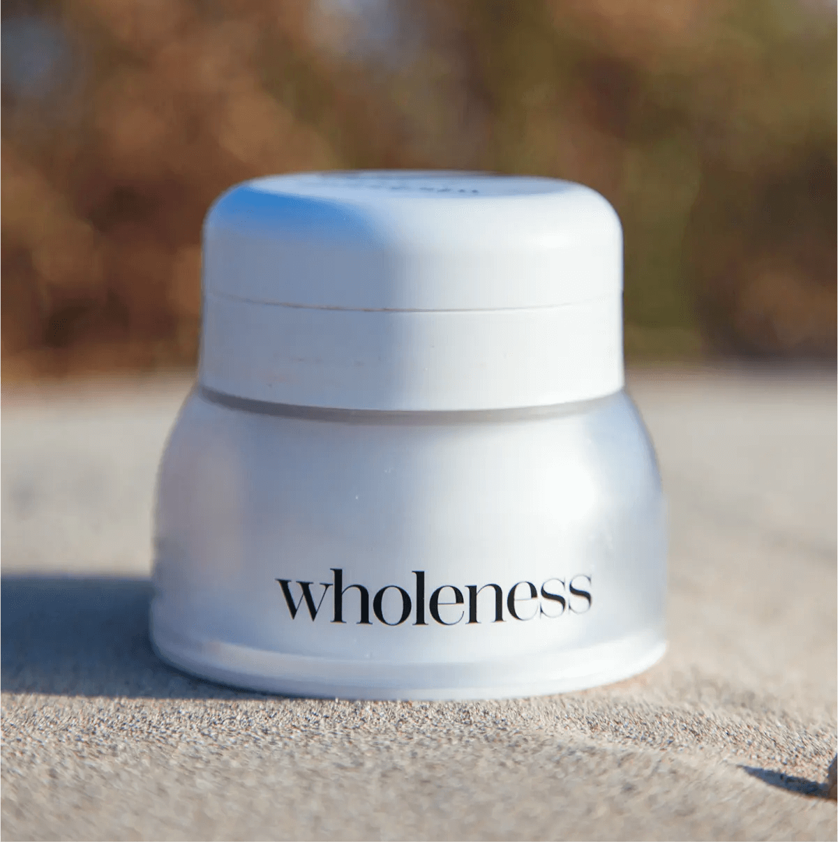White jar labeled 'wholeness' on a sandy surface with a blurred natural background